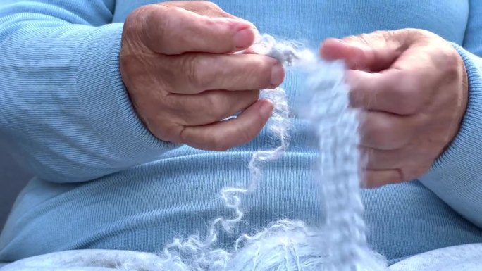 一个手里拿着毛线的女人。老妇人针线活的双手。一个穿蓝衣服的女人解开一条羊毛围巾。
