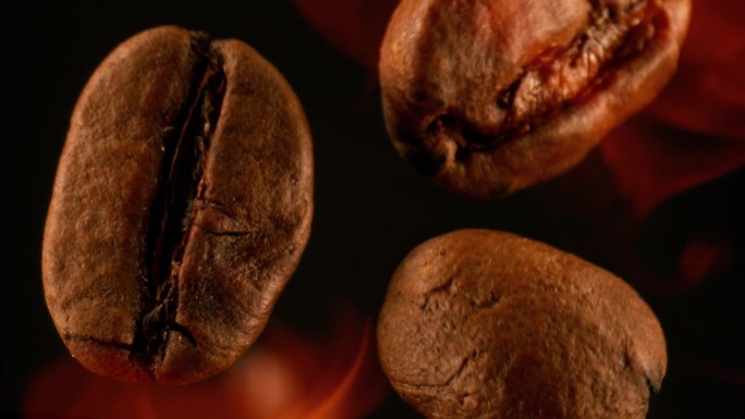 在烤箱中烘烤的咖啡豆落在火焰中，黑色背景上的超级慢动作