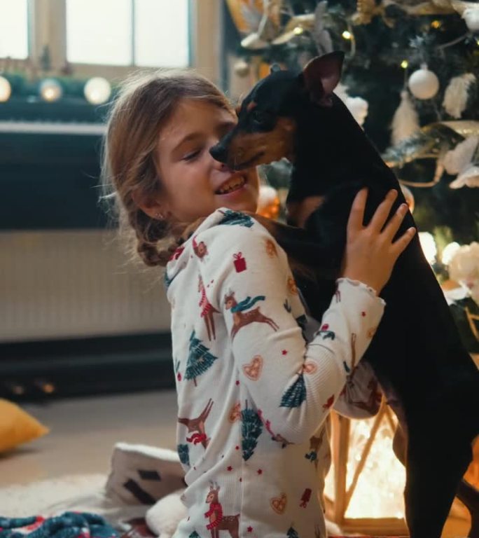 快乐的女孩在圣诞树旁拥抱她的狗狗的垂直照片