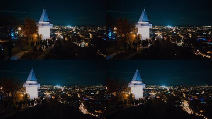 在奥地利格拉茨，人们站在著名的钟楼外，俯瞰灯火通明的城市景观