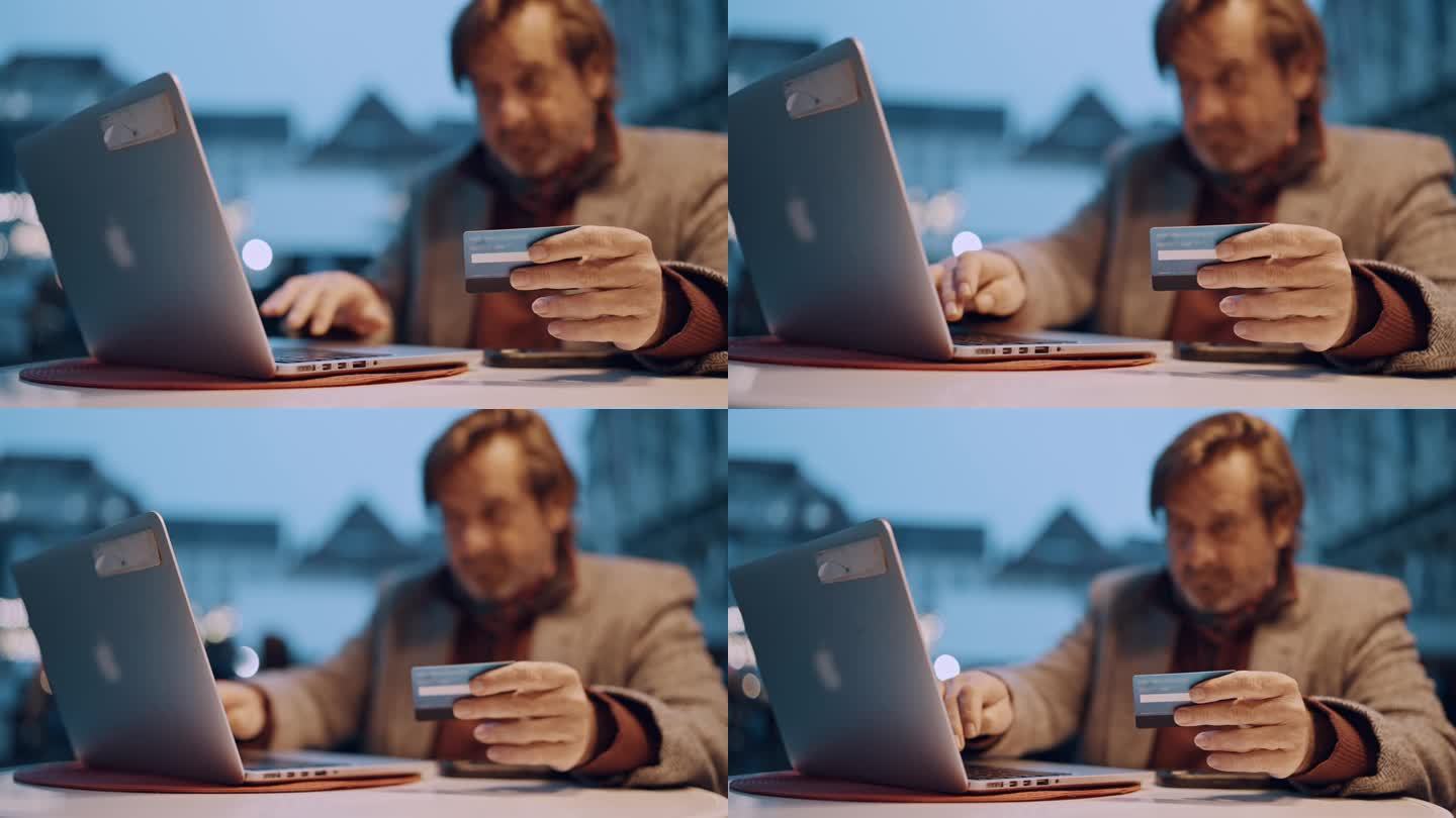 一个成熟的男人拿着信用卡，用笔记本电脑在城市的路边咖啡馆网上购物过圣诞节