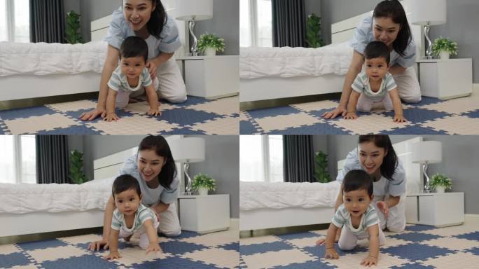 快乐的母亲看着她的婴儿在卧室的游戏垫或拼图地板上爬行