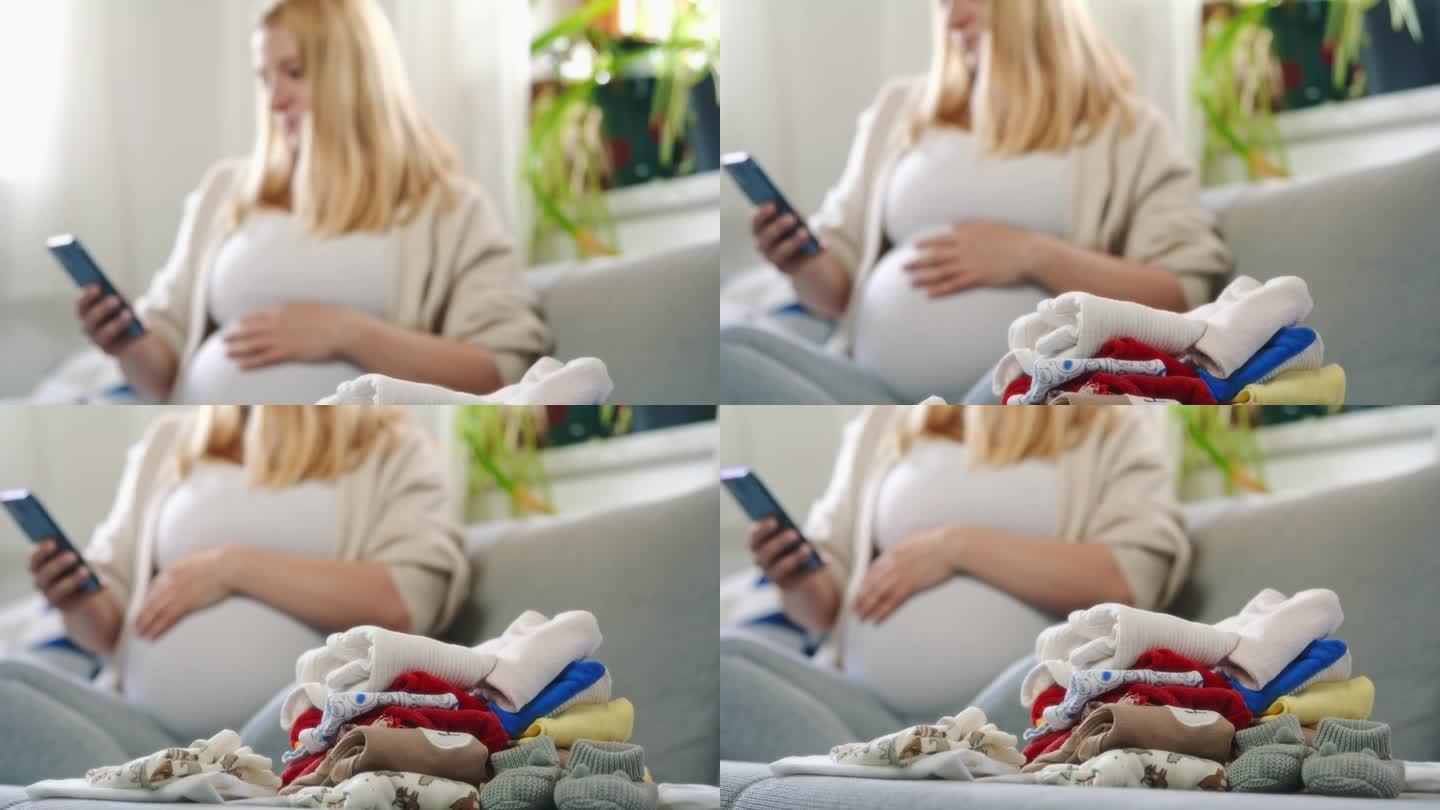 拿着智能手机的孕妇在沙发上叠婴儿衣服