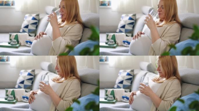 孕妇一边喝水一边在沙发上揉肚子
