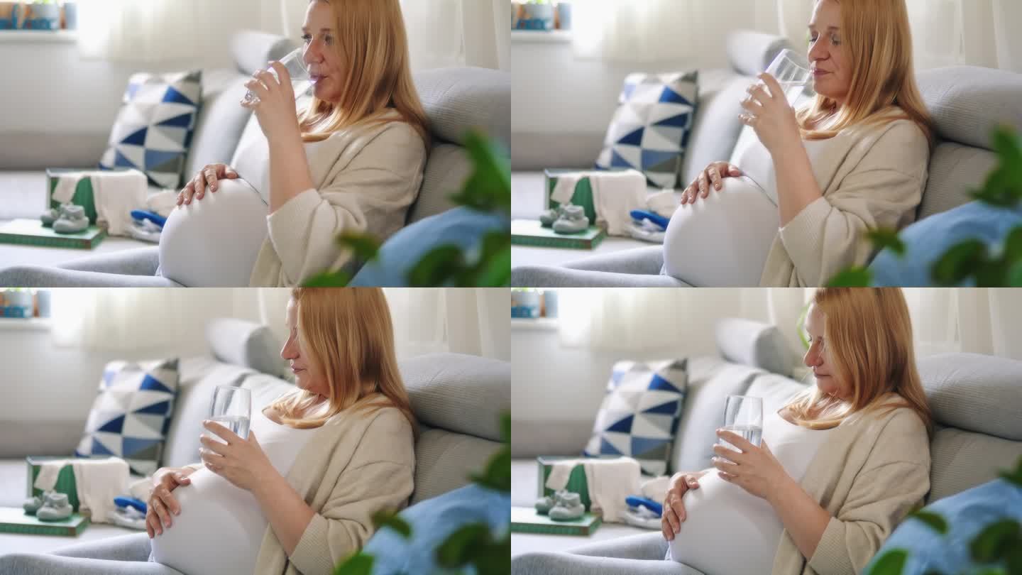 孕妇一边喝水一边在沙发上揉肚子