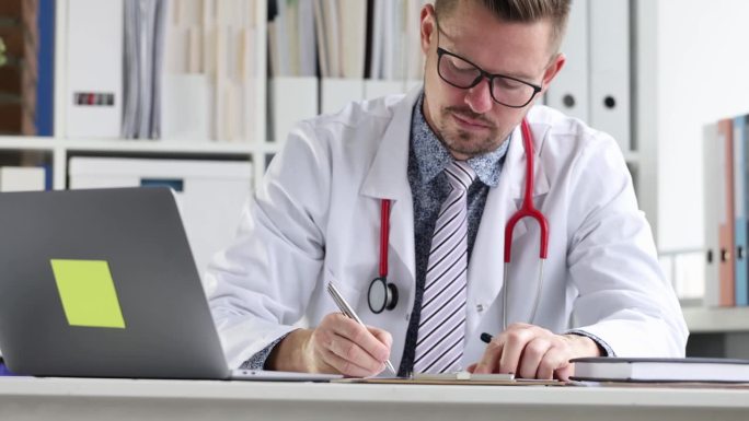 戴着眼镜的年轻医生看着笔记本电脑屏幕，在医疗文件上写4k电影