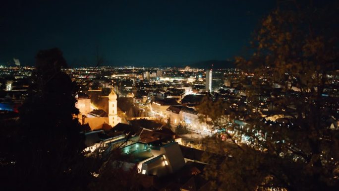 在奥地利施蒂里亚地区的格拉茨，手持航拍的灯火通明的拥挤的城市景观在夜晚的天空中
