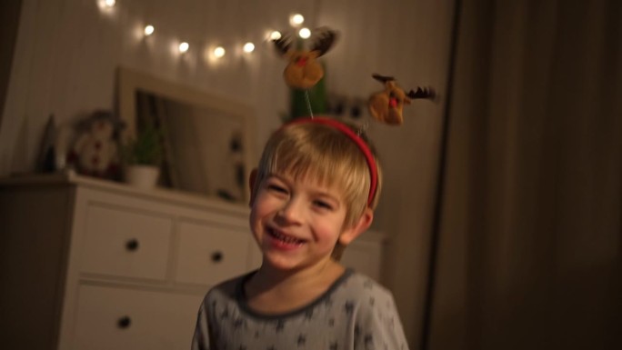 圣诞快乐。有趣的孩子男孩笑着，玩得开心。新年快乐。兴奋的小孩穿着睡衣，在床上跳来跳去，做鬼脸。戴着红