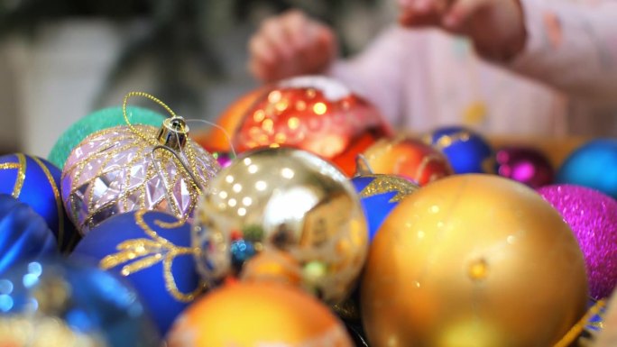 孩子们的手从玩具盒里拿出新年球挂在圣诞树上。一个孩子欢欢喜喜地迎接新年，热情地拆开圣诞树上的一盒装饰