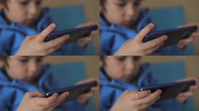 小孩在沙发上玩手机游戏的特写。男孩用手机玩电子游戏。学龄前儿童在沙发上玩电子游戏。孩子用手机玩游戏、