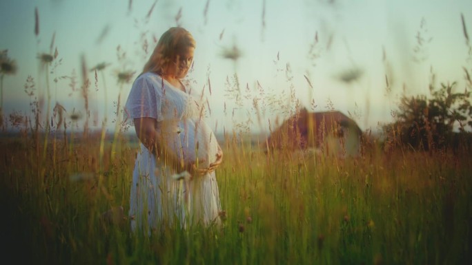 身着白衣的孕妇站在乡间的草丛中
