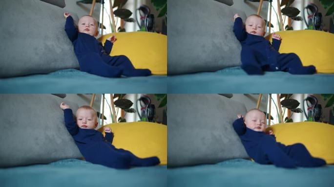 穿着蓝色天鹅绒紧身衣的可爱男婴坐在家里的沙发上