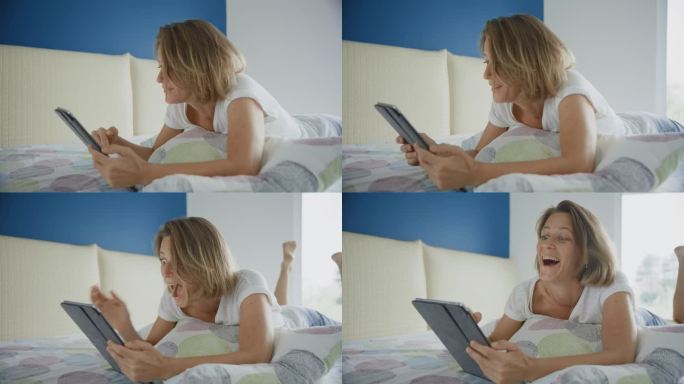 兴奋的女人躺在家里的床上玩着数码平板电脑庆祝成功