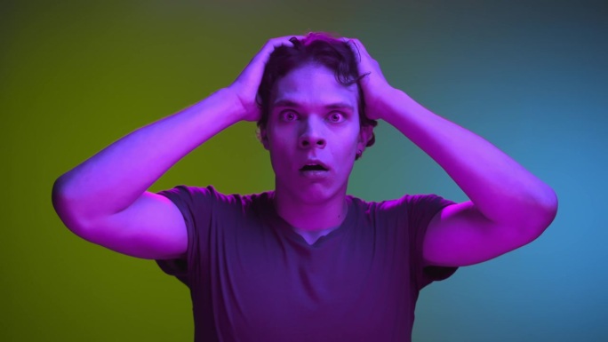 令人震惊的男子近距离看镜头的惊人肖像。可怕的家伙站在霓虹彩色镜头上的黑暗焦虑情绪。在创造性照明的明亮