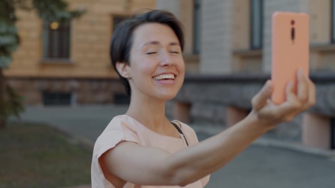 快乐的女孩用智能手机站在城市街道上进行在线视频通话和挥手