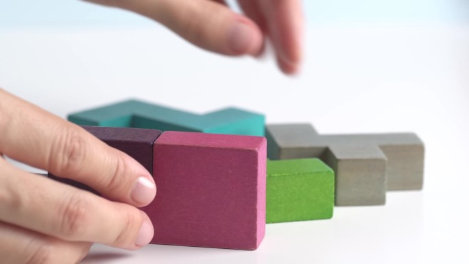 女性手持一块木块拼图。木材立方体堆叠。决策过程的概念，创造性，逻辑思维，聪明的游戏。手工折叠彩色木块