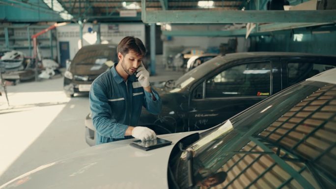 帅气的汽车修理工在车库里用智能手机聊天。拉丁汽车修理工在电话中与客户谈论修车店。