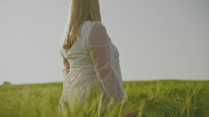 一名孕妇走在农村春天绿色的麦田里