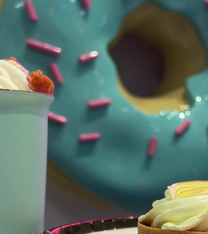 咖啡馆里有饮料和馅饼，背景是一个巨大的蓝色甜甜圈，上面点缀着粉红色的装饰