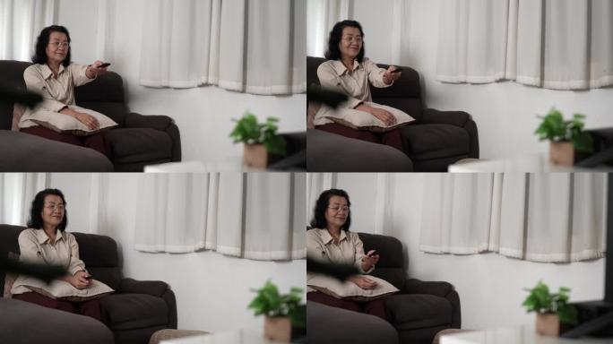老年妇女看智能电视和使用遥控器手持电视音频遥控器中年亚洲妇女电影电视连续剧花时间在家里