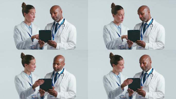 工作室拍摄的男女医生在白大褂与数码平板电脑在白色背景