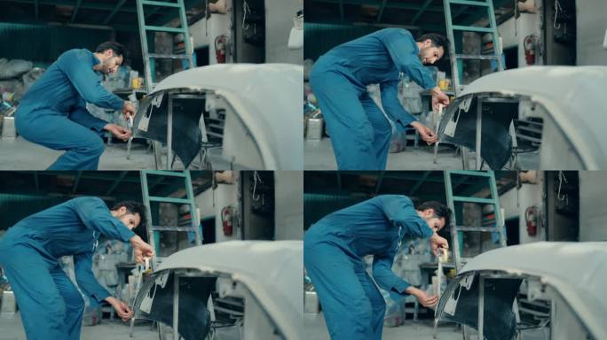 拉丁男技师在汽车车间精密喷漆中使用保护胶带。