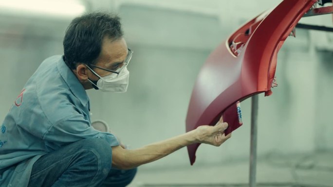 熟练的亚洲技师用喷枪喷漆提高汽车的美观性。