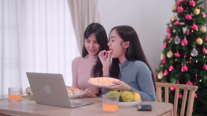 亚洲女性朋友通过笔记本电脑视频通话，在她家的餐桌上与朋友聊天庆祝圣诞节。抓住节日的联系和庆祝。