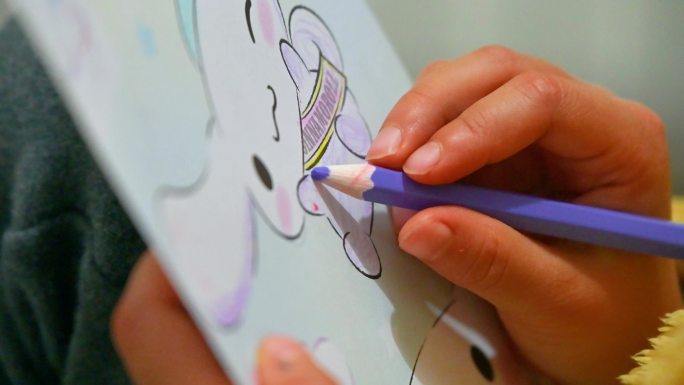 儿童拿着彩笔在绘本上涂画手特写