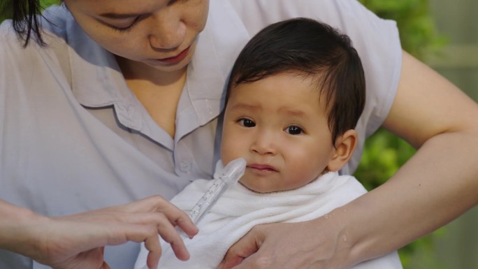 母亲用注射器和生理盐水给婴儿洗鼻水。清洁婴儿鼻子