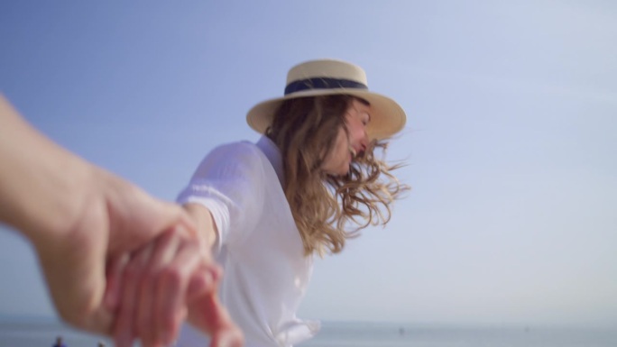 一名女子戴着太阳帽，手牵着手在阳光下的沙滩上奔跑