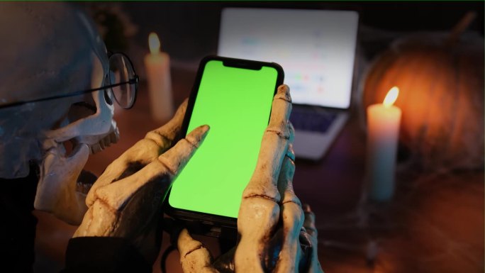 骷髅和穿着骷髅服装的恐怖手拿着绿屏卷轴的手机社交媒体动态，骨指