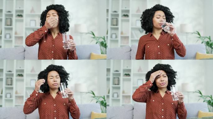 年轻的非裔美国女性坐在沙发上吃止痛药，用玻璃杯喝水