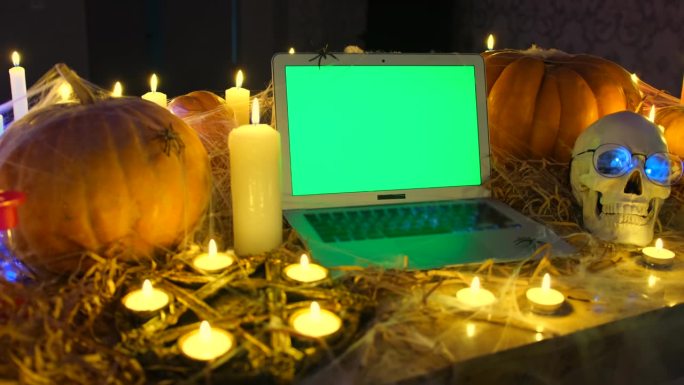 万圣节背景，笔记本电脑与铬绿屏幕，蜡烛，五角星，蜘蛛，和令人毛骨悚然的头骨