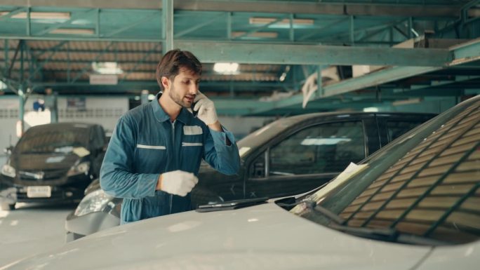 帅气的汽车修理工在车库里用智能手机聊天。拉丁汽车修理工在电话中与客户谈论修车店。