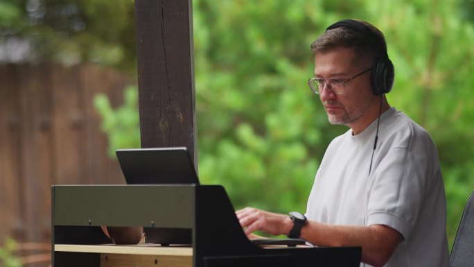 在户外工作。男人戴着耳机听音乐，盯着笔记本电脑屏幕学习