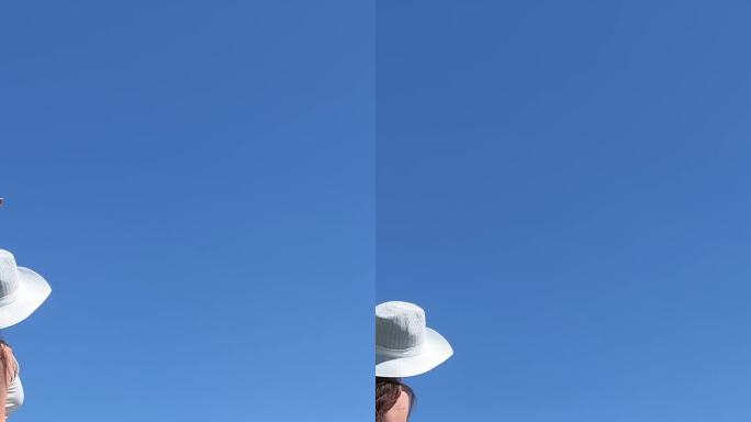 一位戴着白色帽子、身穿白色长裙的游客向一架飞向他的飞机挥手。在女孩的旁边有一个巨大的蓝色手提箱，颜色