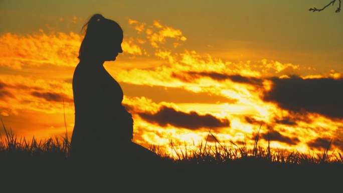 孕妇抱着婴儿肚子映衬着日出的天空