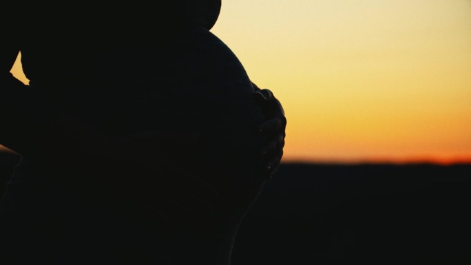 在日出的田野里，孕妇抱着肚子的剪影