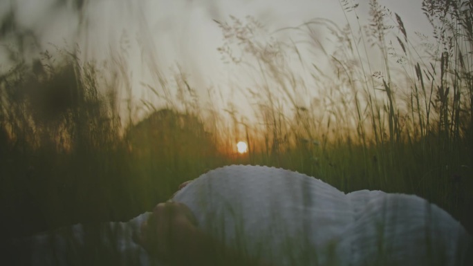 日出时，孕妇躺在田园诗般的田野里放松。草地上的孕妇。