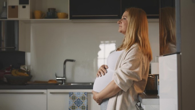 体贴的孕妇在厨房按摩肚子
