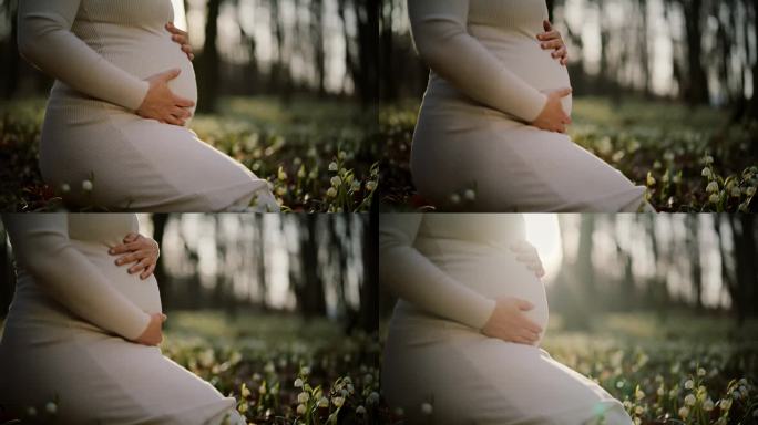 特写:一名身穿白衣的孕妇在树林里抱着肚子