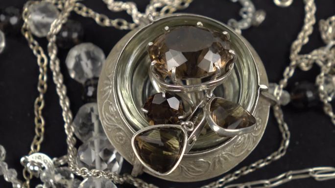 银戒指与烟熏石英，复古项链，由切割的岩石水晶和烟熏黄玉放置在黑色的布。