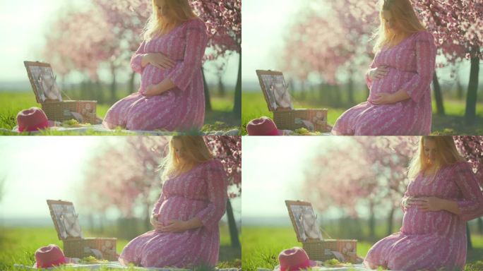 身穿粉色连衣裙的孕妇在春天的果园里野餐