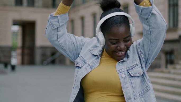 细心的非洲裔美国妇女戴着耳机在户外跳舞，在城市街道上玩耍