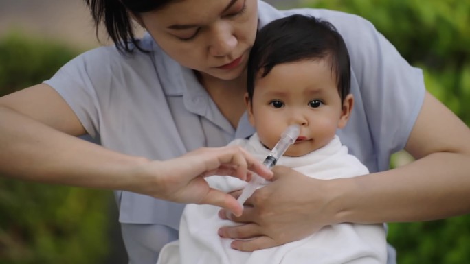 母亲用注射器和生理盐水给婴儿洗鼻的慢动作。清洁婴儿鼻子
