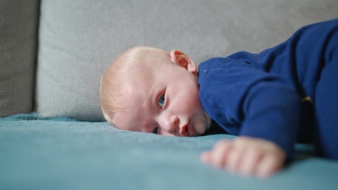可爱的小男孩穿着蓝色天鹅绒紧身衣倒立在家里的沙发上