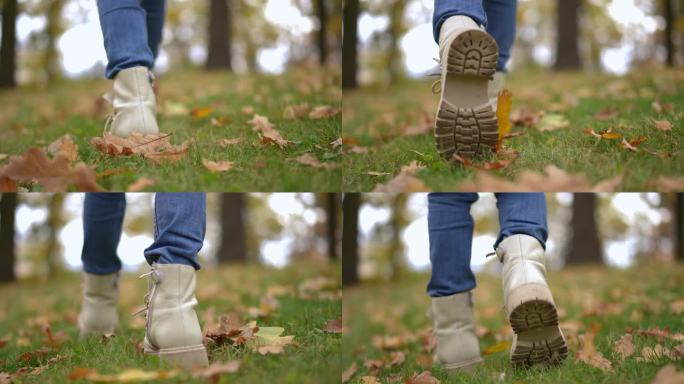 在草地上的秋天公园里，现场摄像机跟随一个穿着白色靴子的女孩的脚慢动作行走。后视图跟踪拍摄的孩子漫步在