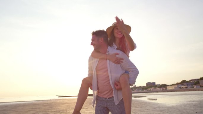 在阳光明媚的海滩上，一个男人背着他的妻子，一边旋转一边笑