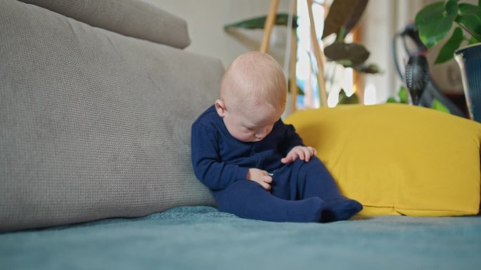 睡意朦胧的小男孩穿着蓝色天鹅绒紧身衣倒在家里的沙发上